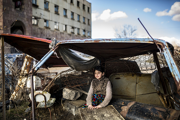 Nine-year-old Suzanna sitting in a “shelter” made of old car rusty parts ten days after her father committed suicide (Photo: Yulia Grigoryants)